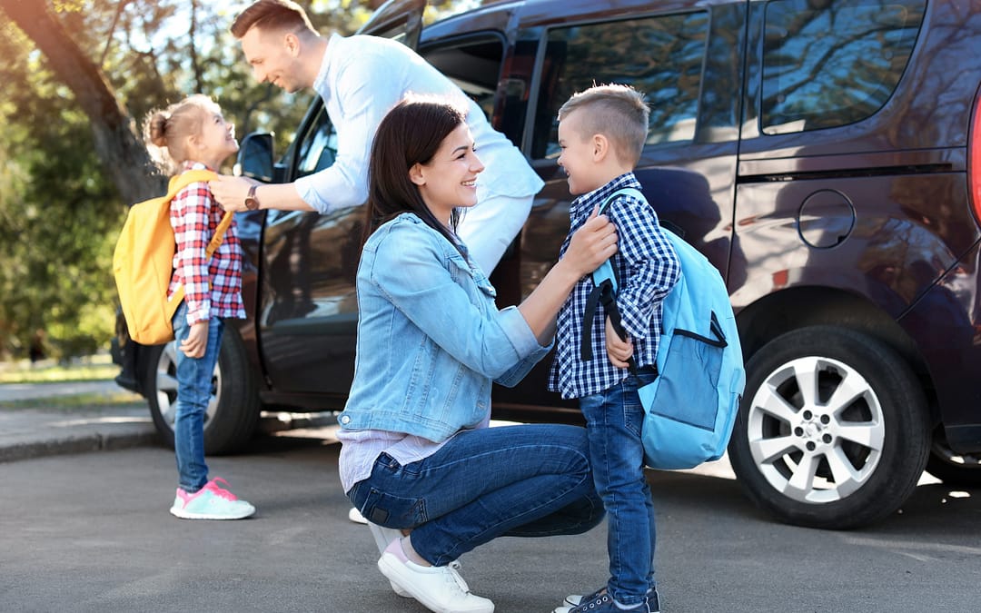 Young Parents Saying Goodbye To Their Little Children Near School